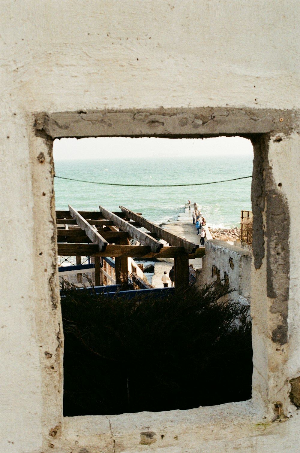 a stone archway with a view of the ocean and people walking on it