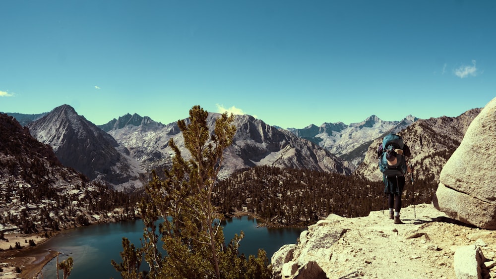 a person standing on a rocky ledge overlooking a lake and mountains