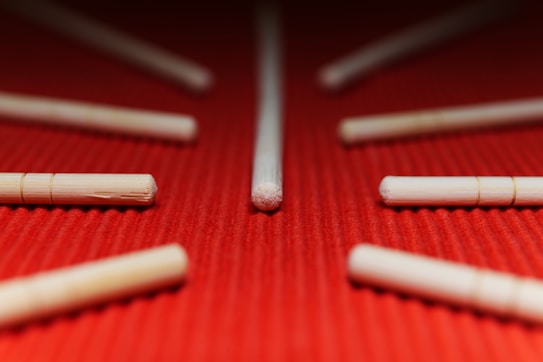 Several wooden sticks are arranged on a textured red surface, with one central stick prominently placed in the middle.