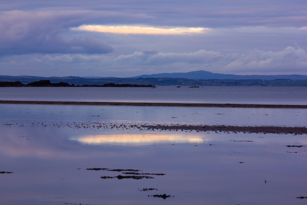 a body of water with a beach and mountains in the background