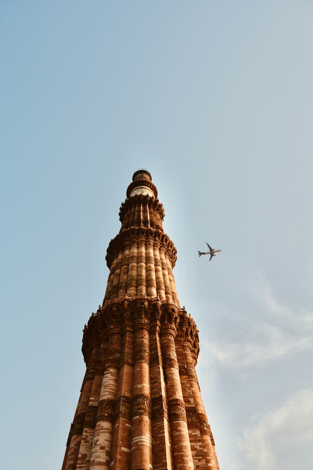 a plane flying over a tall tower with Qutub Minar in the background