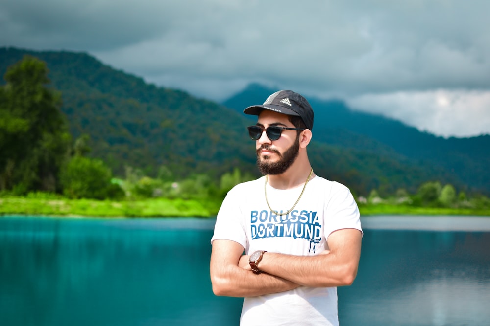 a man standing by a body of water with trees and mountains in the background