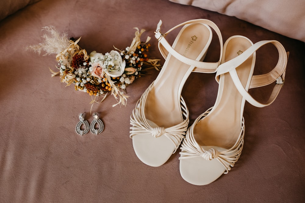 a pair of white sandals with gold jewelry on a pink surface