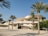 A modern architectural structure with a unique, curved design resembling desert rose formations. Palm trees are positioned in the foreground amidst a clear blue sky, adding a touch of greenery to the scene.