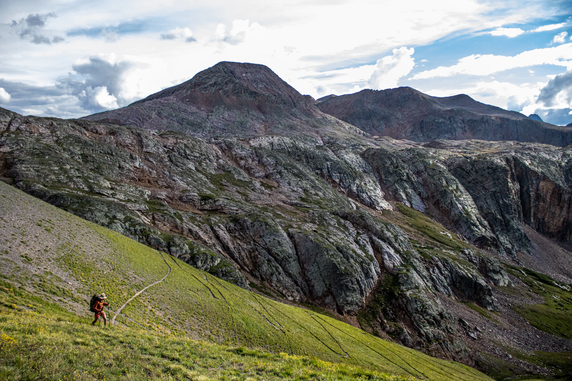 A hiker following a winding trail through the San Juan Mountains