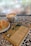 A cup of latte art coffee, a sesame-topped pastry on a white plate, and a book titled 'Las Siete Leyes Espirituales del Éxito' by Deepak Chopra are placed on a patterned, tiled table. The background shows a foggy, possibly rainy window.