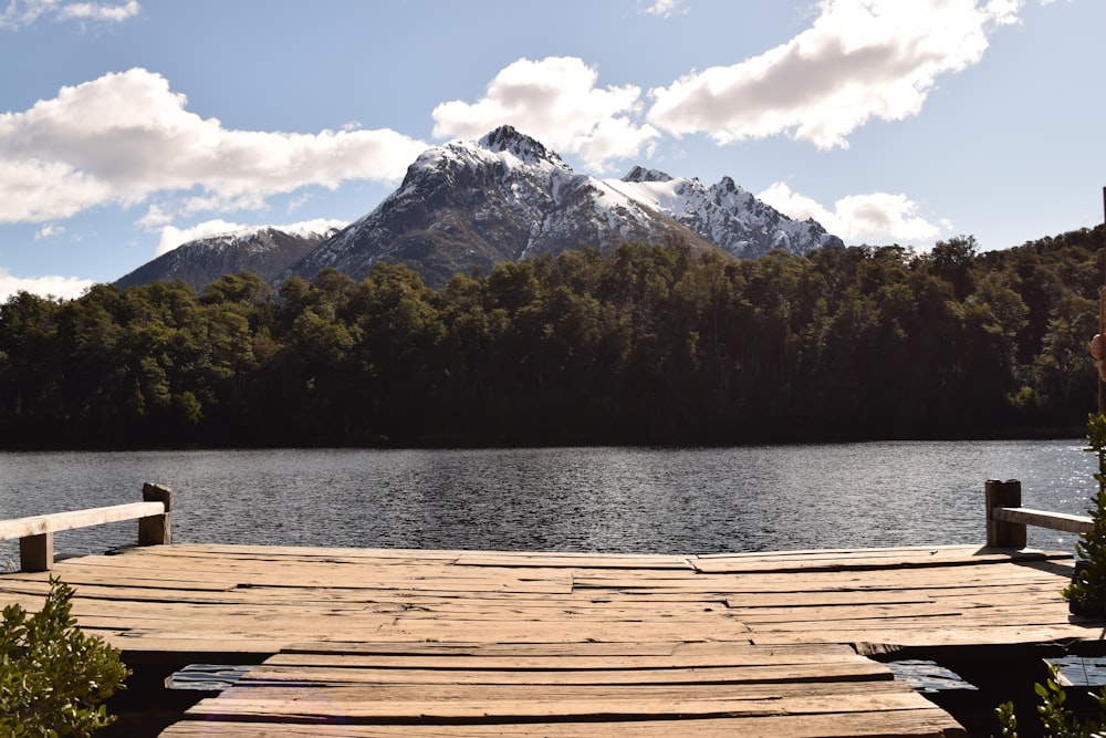 uma doca de madeira que leva a um lago com uma montanha ao fundo