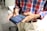 A person wearing a red, blue, and white plaid shirt, holding a smartphone. The phone screen displays a messaging application. The background shows an office environment with desks and chairs.