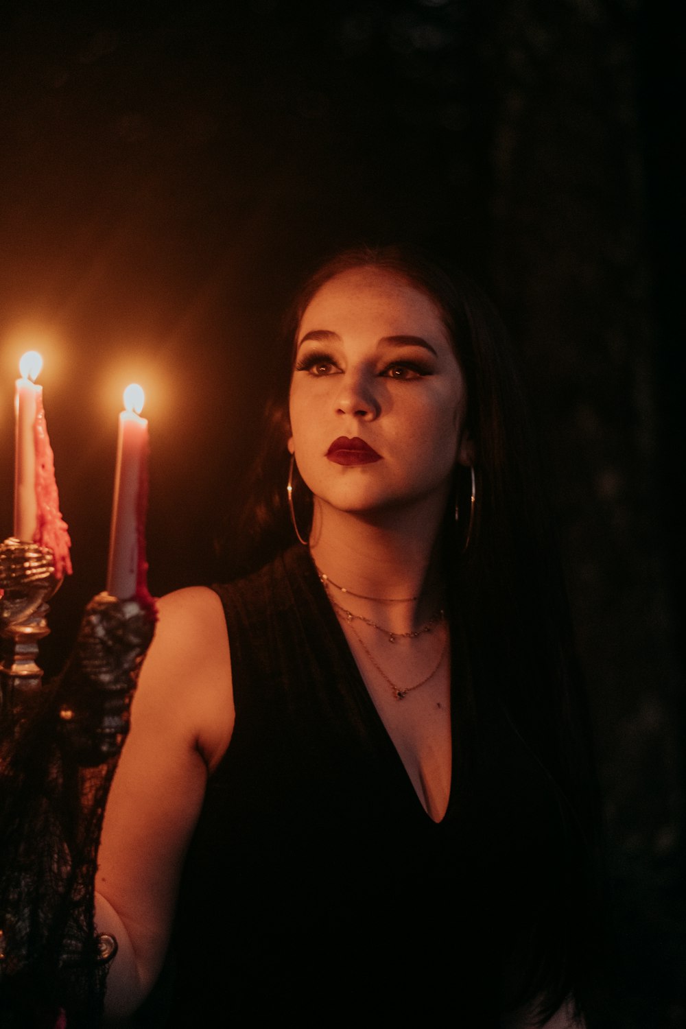 a person with a necklace and a black dress with candles in the background