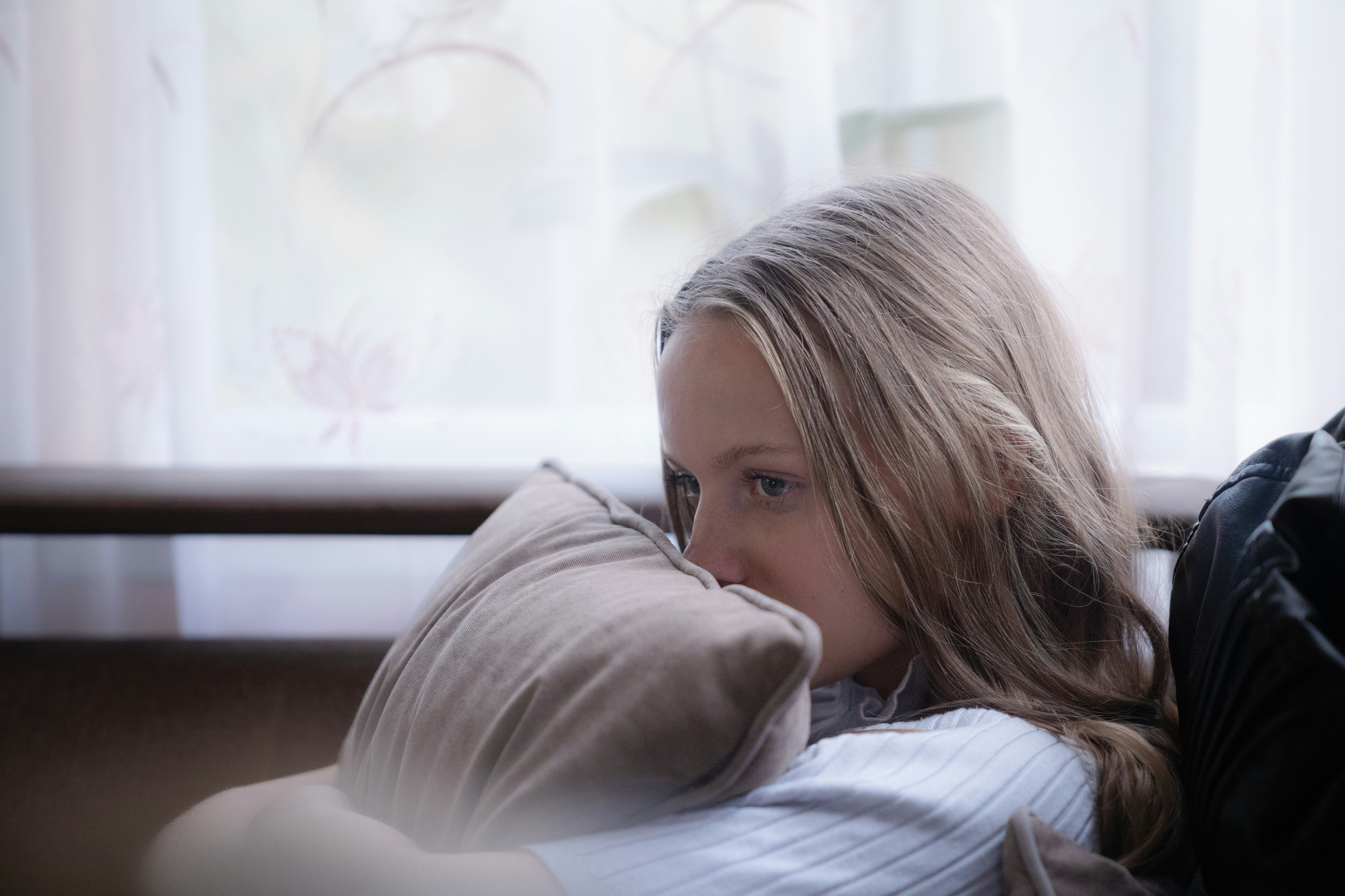 a girl with blonde hair hugging a pillow.