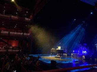 Luxurious music venue stage with golden spotlights and a man in a tailored black suit tuning instruments.