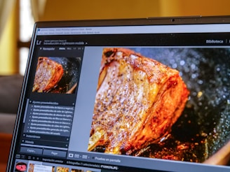 A laptop screen displaying Adobe Lightroom Classic software with a close-up image of a cooked piece of meat being edited. The interface shows various editing options and a navigation panel on the left side.