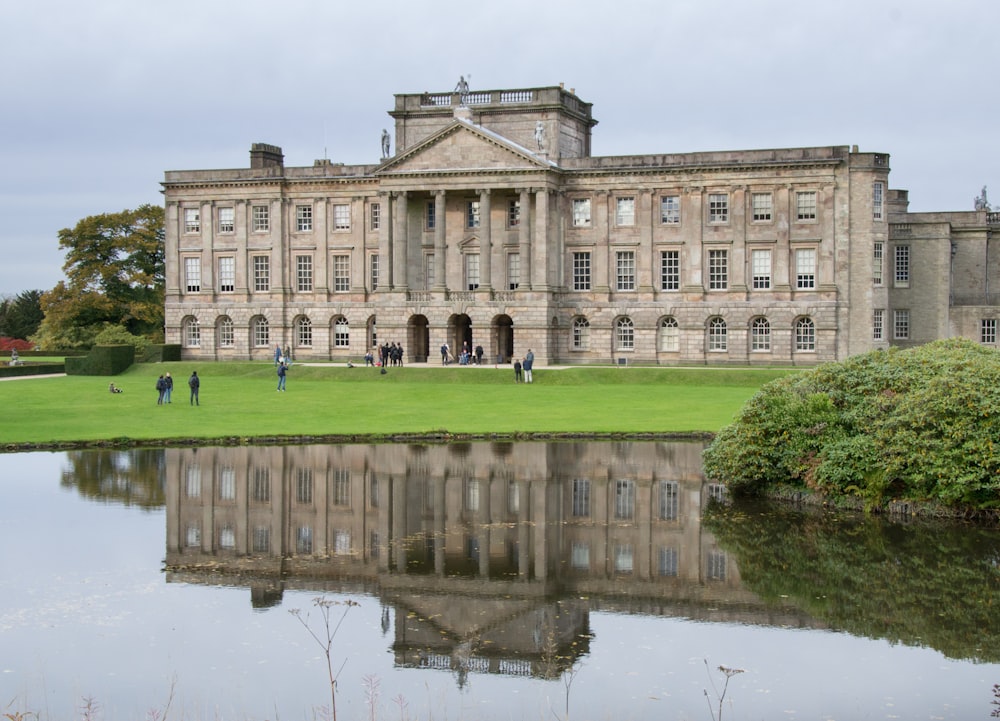 a large building with a pond in front of it with Lyme Park in the background