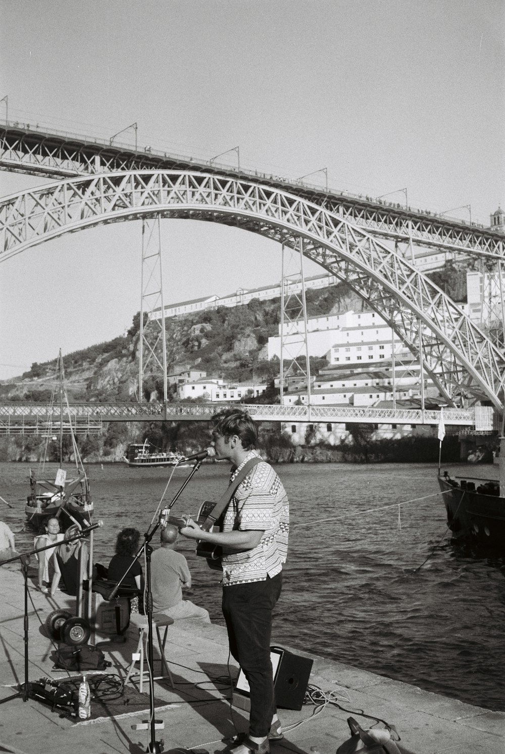 a man playing a guitar on a boat in front of a bridge