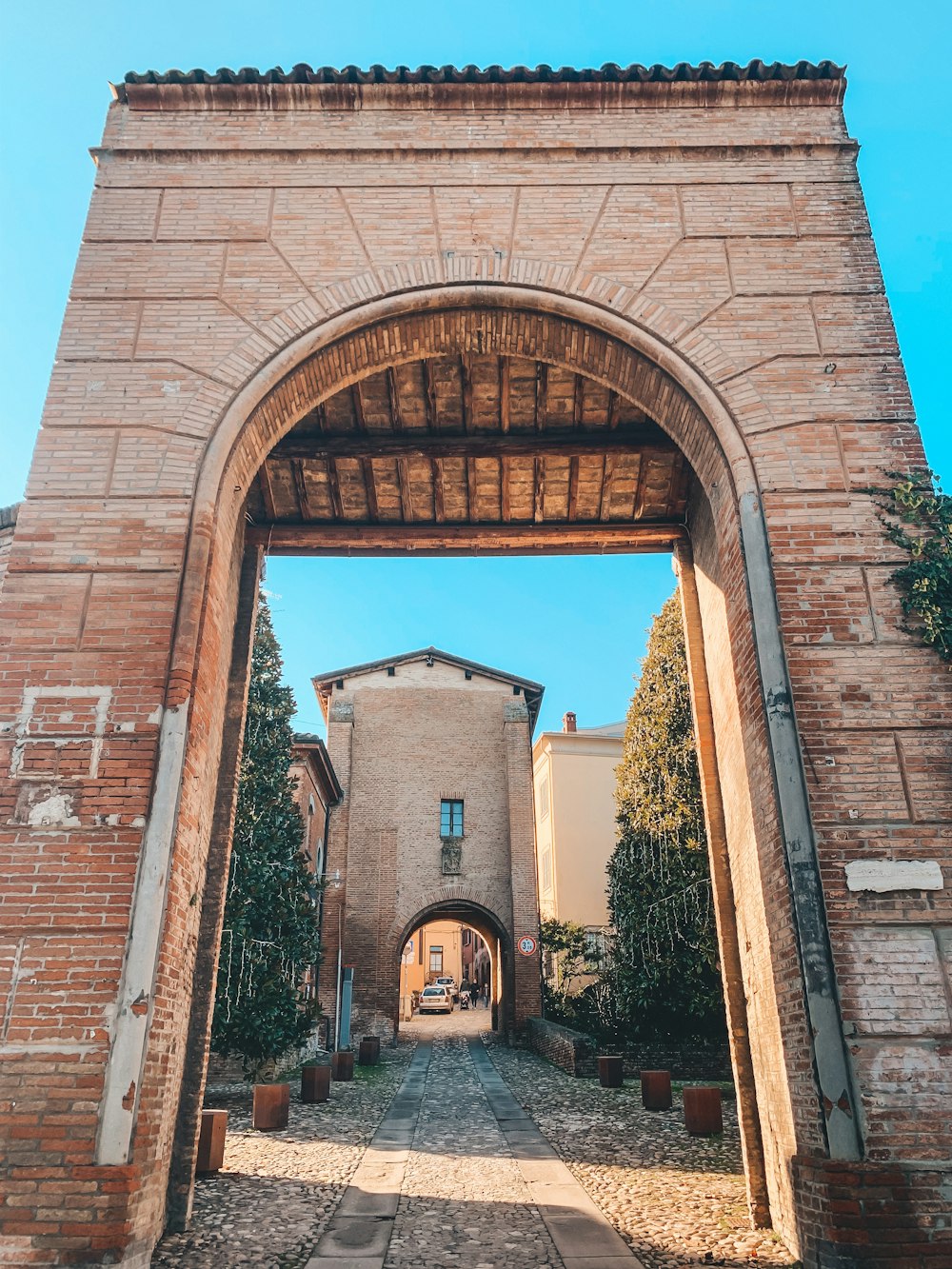 a brick archway with trees and a building in the background