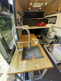 Technicians installing kitchen equipment and plumbing inside a box truck conversion.