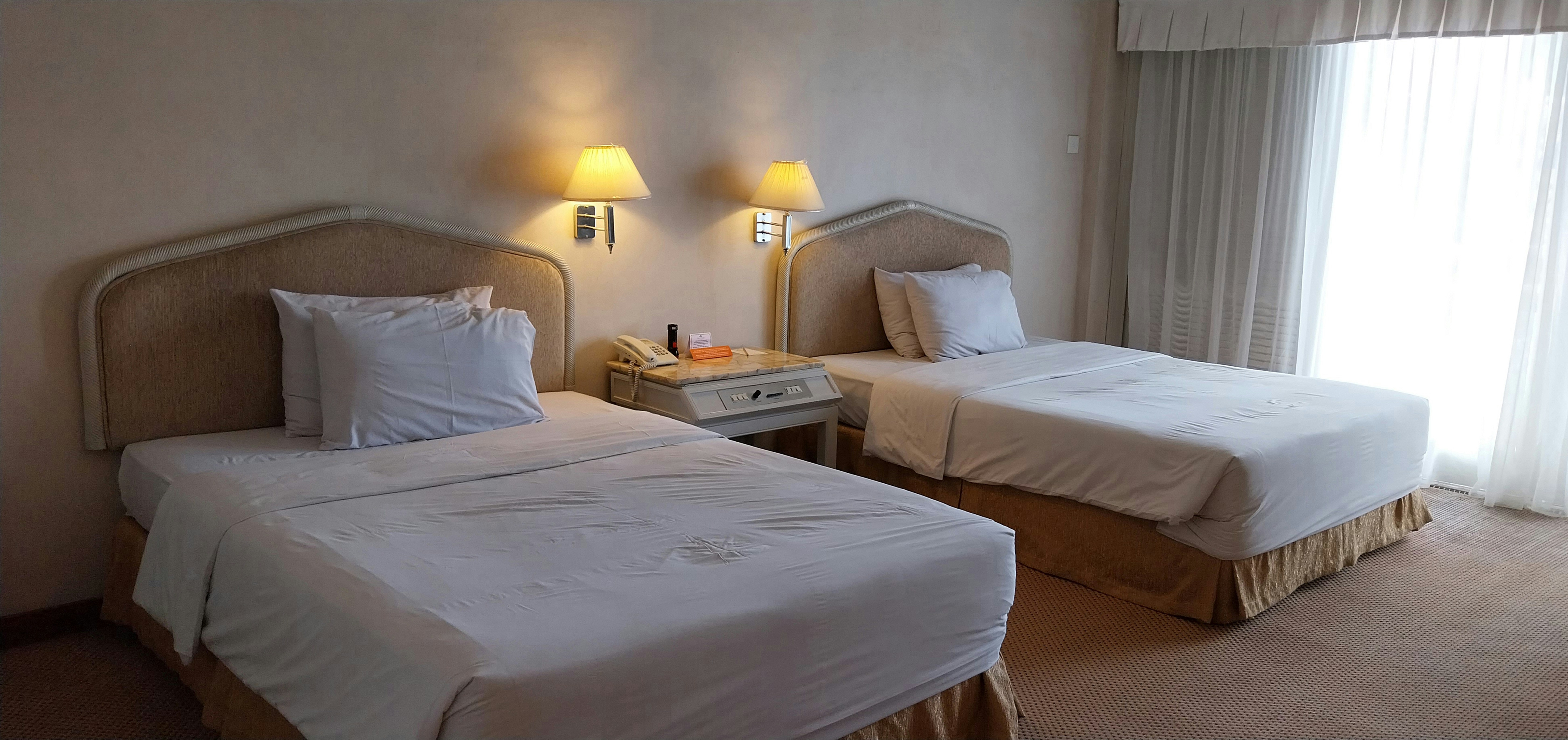 Clean standard hotel room with white bedding, AC unit, and warm lighting in compact layout