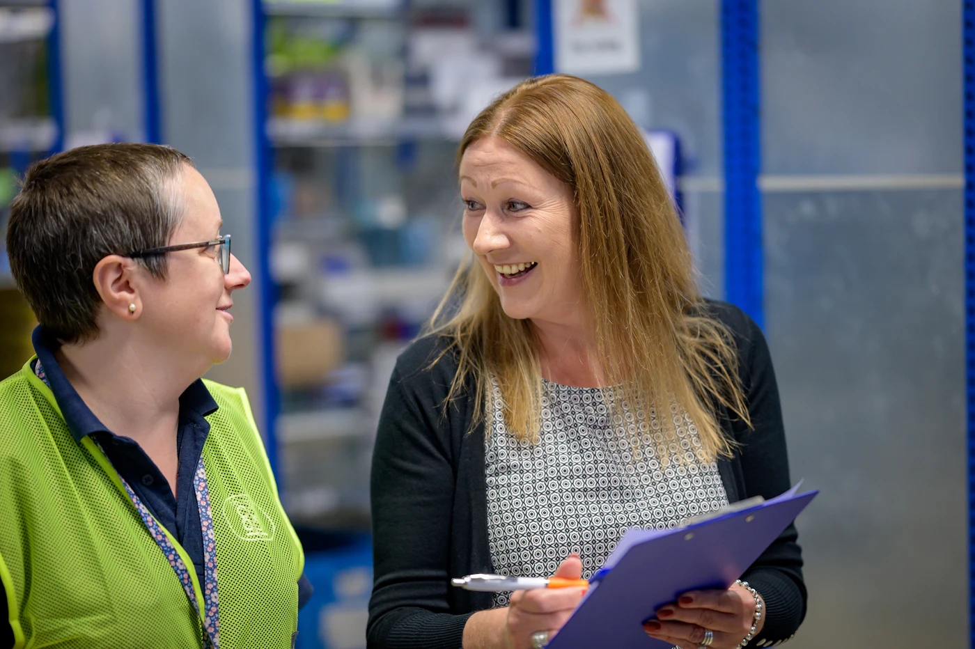 Warehouse supervisor talking through a process with a team member in a safety vest on the warehouse floor