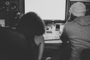 a man and woman sitting at a desk looking at a screen