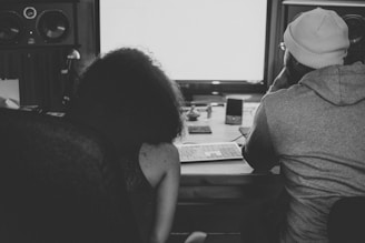 a man and woman sitting at a desk looking at a screen