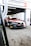 A racing car with a black, red, and white color scheme is positioned in a motorsport garage under a sign that reads 'Century Motorsport BMW M4 GT3'. The car has various brand stickers, including Sonax and Pirelli, and is partially outside the garage ready for a race.