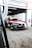 A racing car with a black, red, and white color scheme is positioned in a motorsport garage under a sign that reads 'Century Motorsport BMW M4 GT3'. The car has various brand stickers, including Sonax and Pirelli, and is partially outside the garage ready for a race.