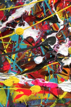 An abstract composition featuring bold, swirling patterns and chaotic splashes of color. The vibrant colors blend and intersect with various shapes and textures, creating a dynamic and energetic visual impact.
