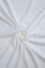 Delicate ivory lace fabric draped softly over a satin surface in warm, natural light.