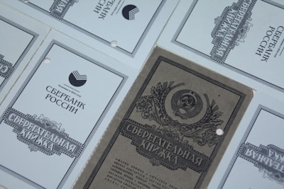 Multiple documents are arranged with a design featuring Cyrillic text and emblems, suggesting financial or official papers. The central document has decorative elements, including an emblem with a shield and foliage.