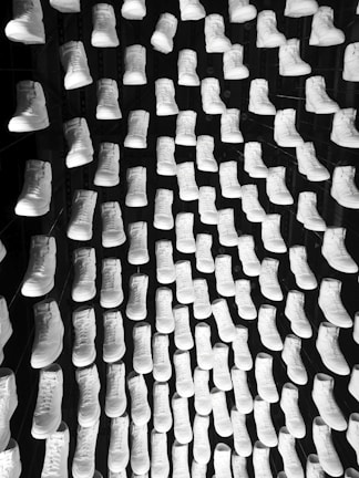 A symmetrical display of numerous pairs of white sneakers arranged in a grid pattern against a dark background. The shoes are uniformly oriented, creating a visually striking and orderly composition.