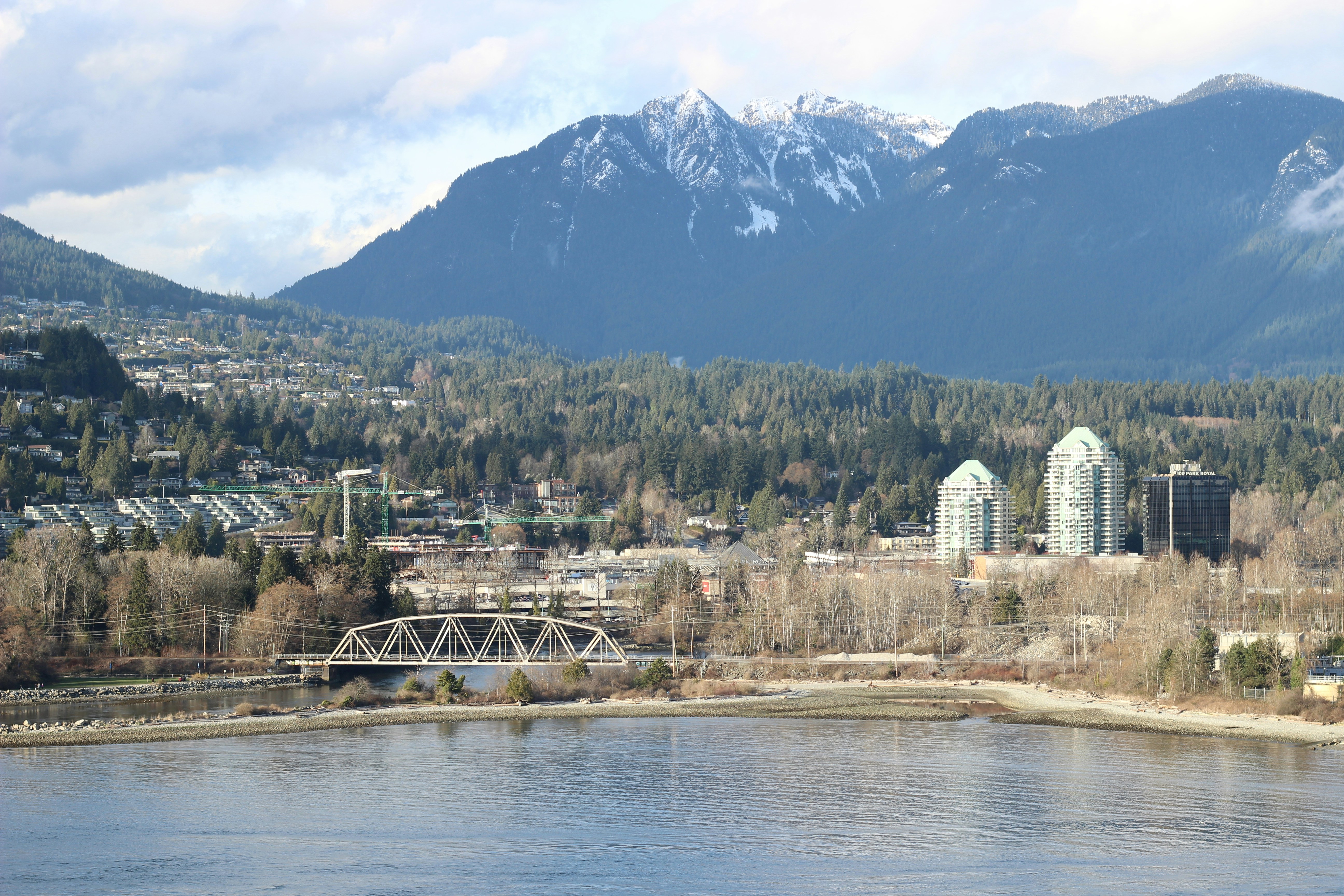 City buildings and bridge by a lake with mountains.