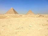 Ancient pyramids standing tall under a bright blue sky, surrounded by desert landscape.