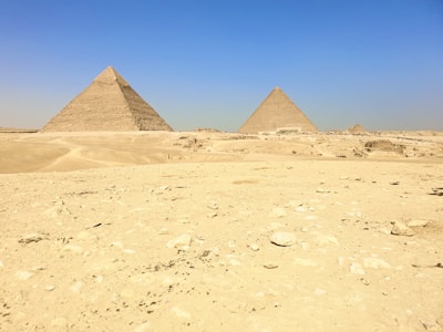 Ancient pyramids standing tall under a bright blue sky, surrounded by desert landscape.