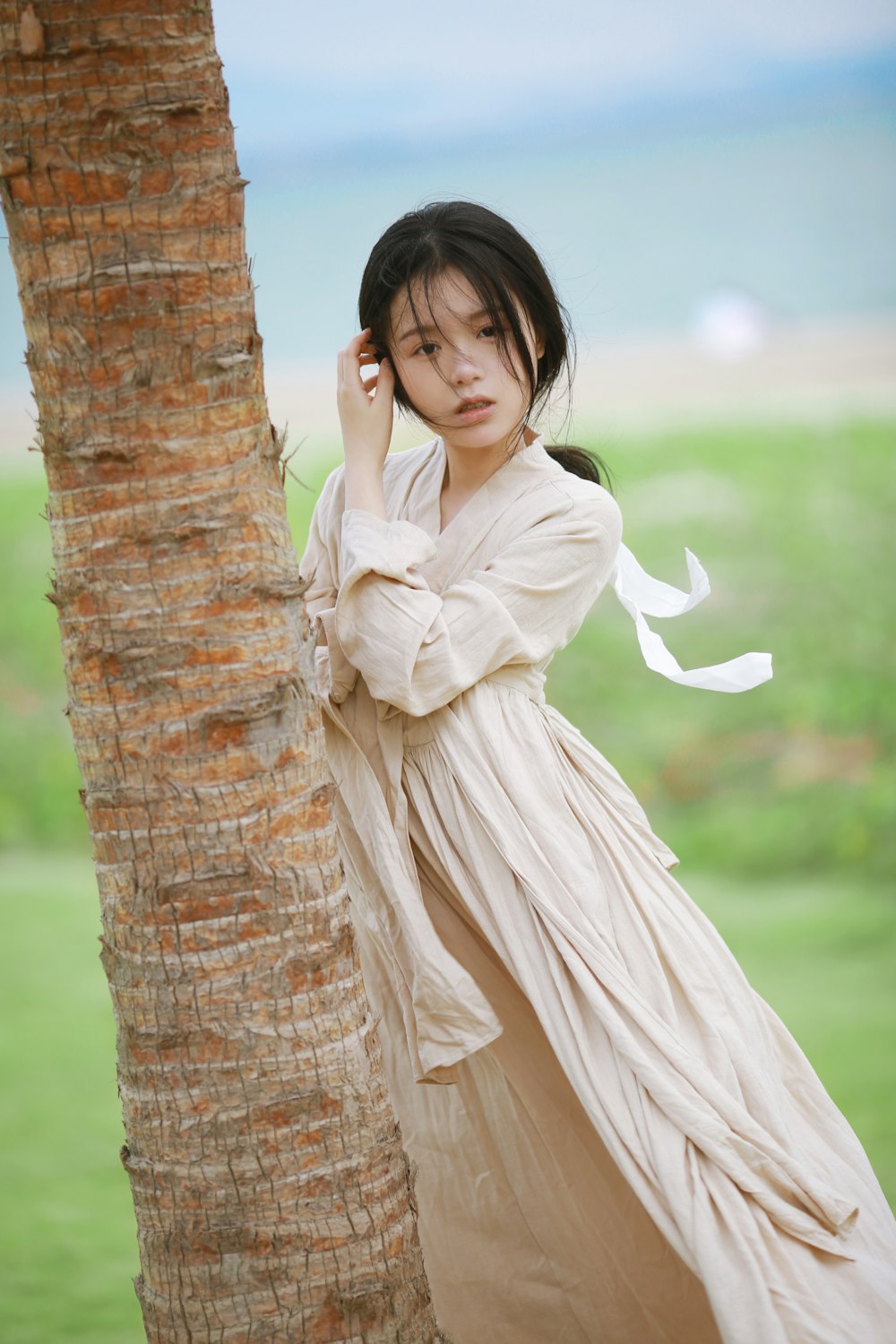 a person in a white dress leaning against a tree