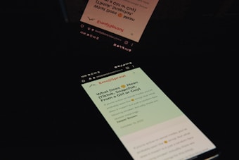 A smartphone screen displaying an article from a website named Emojipedia, reflecting on a dark surface. The article seems to discuss the meaning of certain emojis on social media platforms such as TikTok and Snapchat. The display is primarily in English with some graphical icons indicating webpage features like sharing and menu.