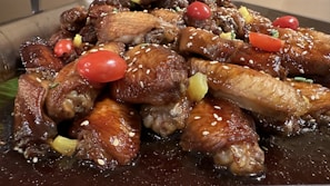 A platter of fried chicken wings glazed with a spicy sauce, garnished with chopped herbs