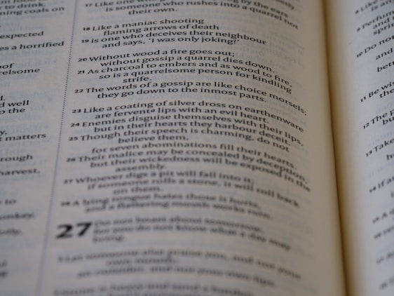 Text from an open book with several verses written in a poetic format, highlighting words about gossip and deceit. The page is focused, while the surrounding area is slightly blurred, suggesting depth.
