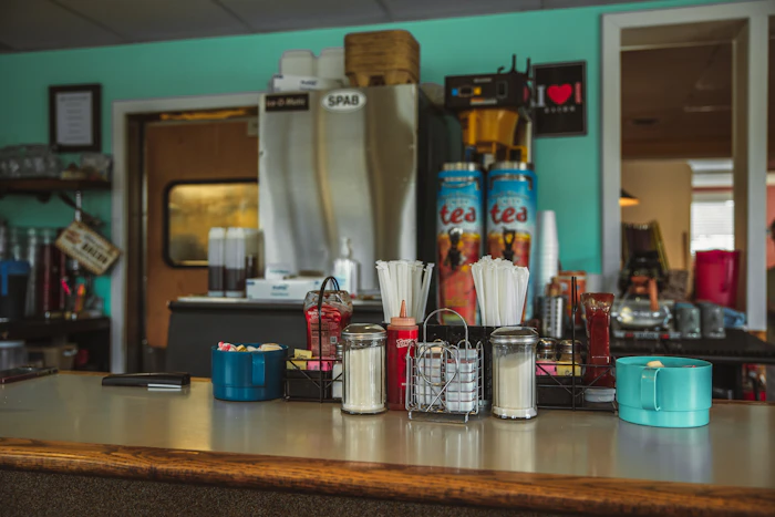A cup of fresh diner coffee on a saucer beside a chrome napkin holder.