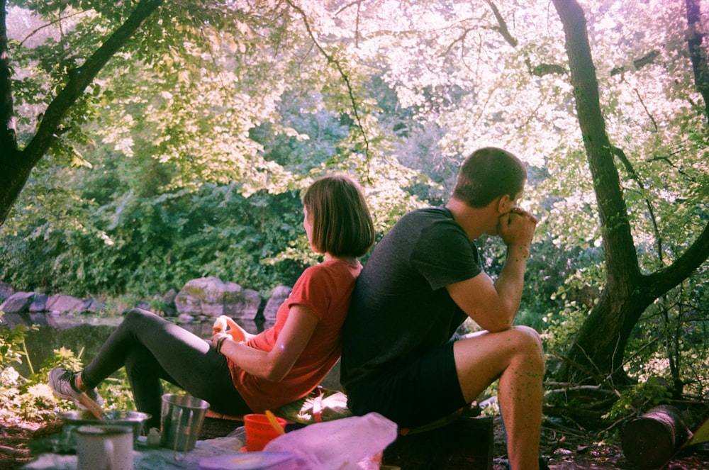 a man and woman sitting on a blanket in the woods