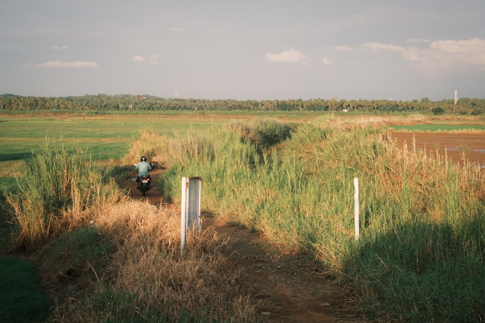 a person riding a motorcycle on a dirt path in a field