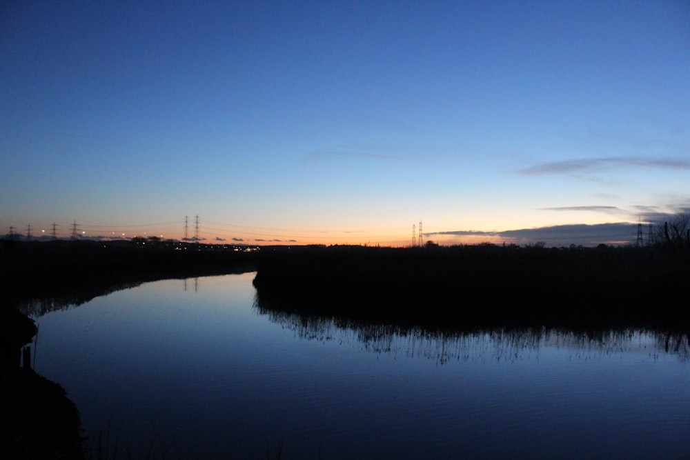 a body of water with trees and a sunset in the background