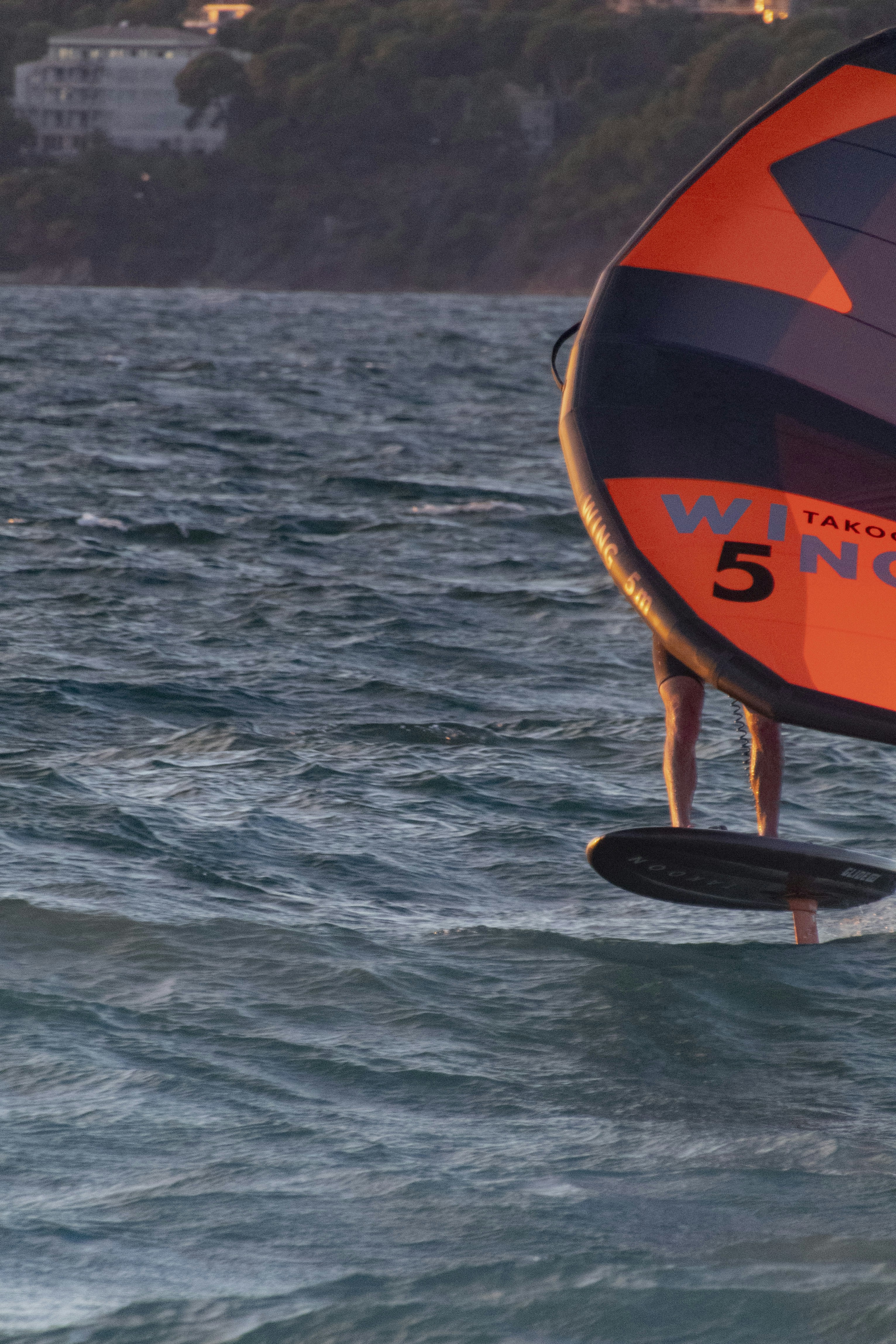 Wingfoiler naviguant sur une mer formée au coucher du soleil