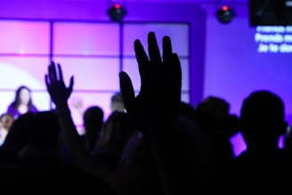 Close-up of hands raised in worship, glowing softly against a deep royal purple backdrop.