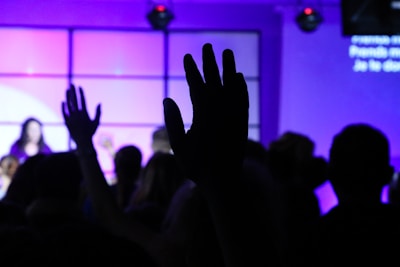 Close-up of hands raised in worship, glowing softly against a deep royal purple backdrop.