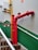 A bright red firefighting pipe system is installed along a staircase with green and white walls. The pipes include prominent valves and connectors, and a yellow gas pipe runs parallel to the firefighting system. The stairs have wooden steps and white railings.