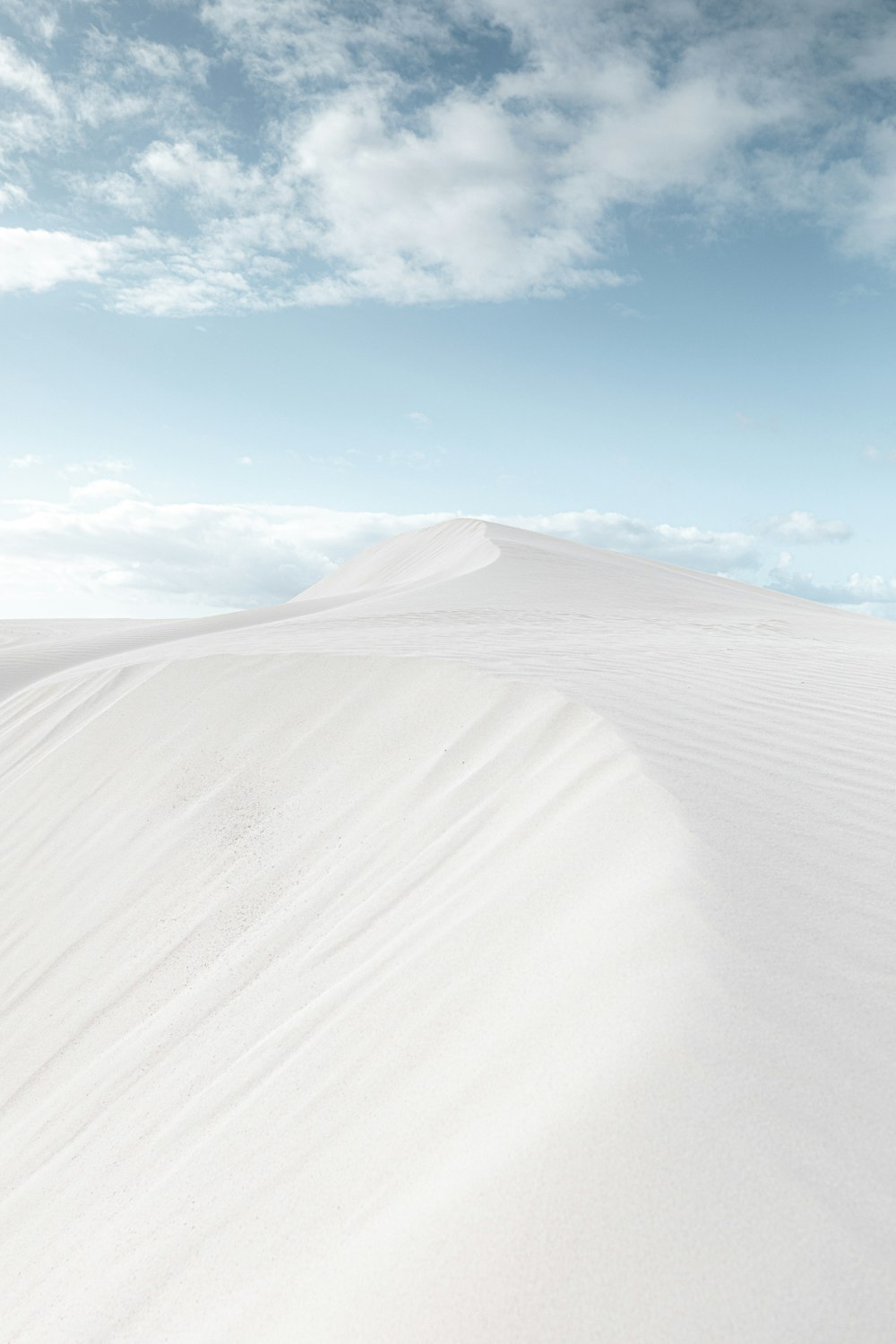 a large flat area with clouds above with White Sands National Monument in the background