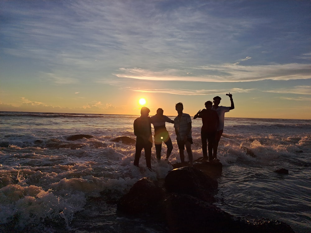 a group of people standing on a rock in the water with the sun setting