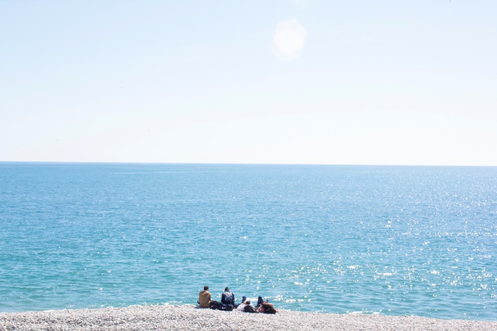 a group of people sitting on a beach by the water