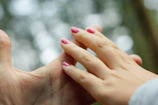 Close-up of gentle hands applying holistic therapy with blush pink background.