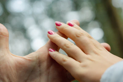 Close-up of gentle hands applying holistic therapy with blush pink background.
